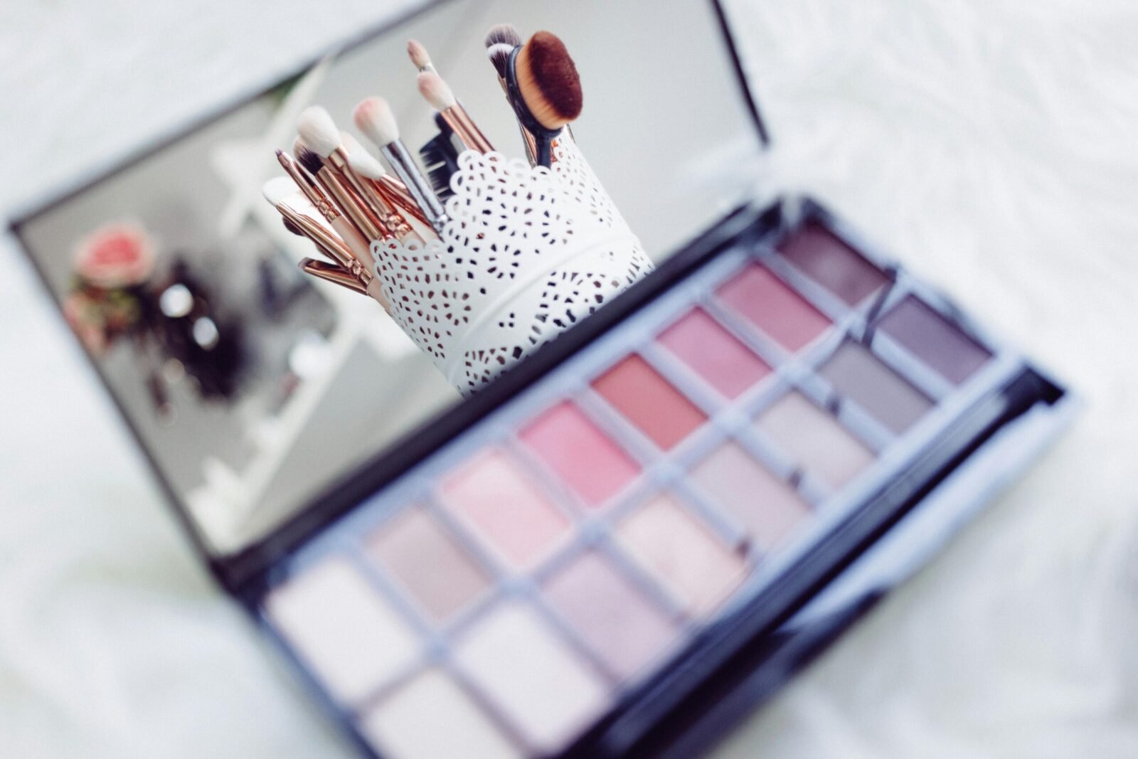 Close-up of makeup brushes in a decorative holder and a colorful eyeshadow palette.