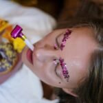 Vibrant makeup and festive scene with glitter eyebrows, party blowers, and tasty doughnuts.