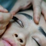 A close-up image of a makeup artist applying eyeliner to a woman's eyelid with precision.