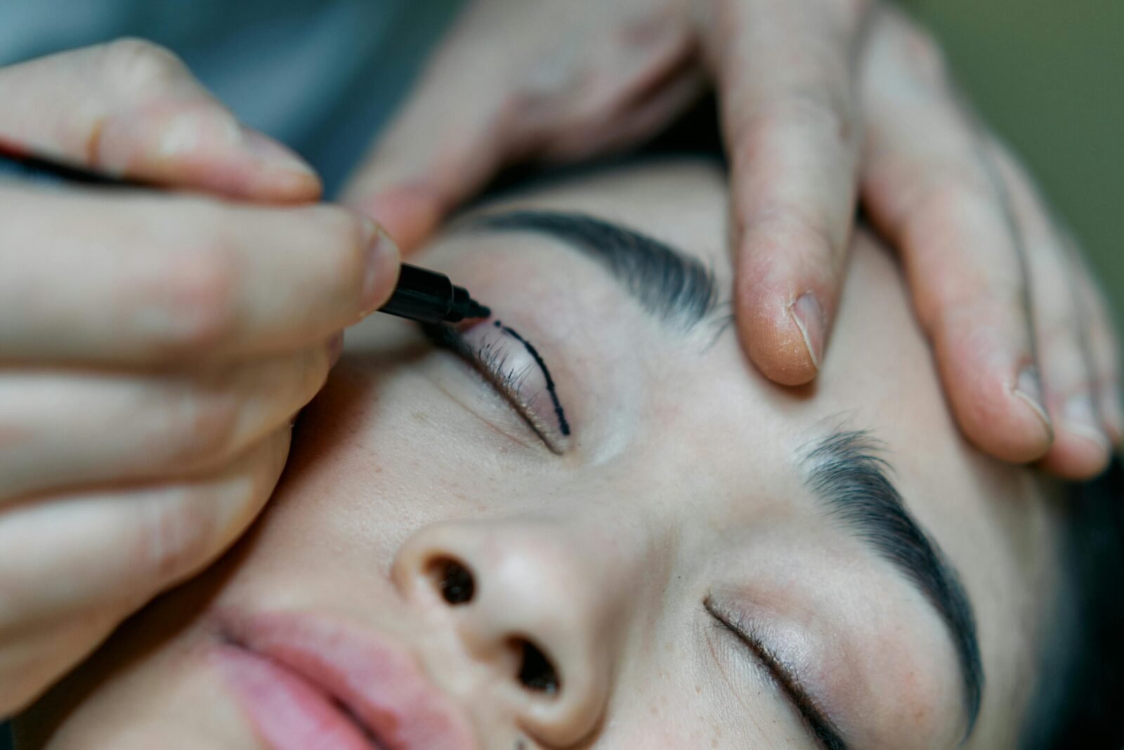 A close-up image of a makeup artist applying eyeliner to a woman's eyelid with precision.